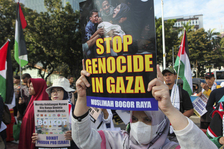 Protester holds a sign accusing Israel of genocide in the Gaza war—a common blood libel readily disproven by hard facts, including Israel’s unmatched efforts to protect and feed enemy civilians, as well as death-toll demographics reflecting focused targeting of fighting-age males. 